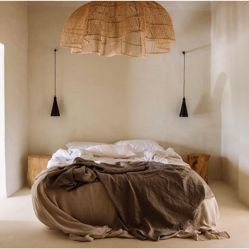 Suspension CÉLESTE XXL en rotin naturel dominant un lit dans une chambre épurée